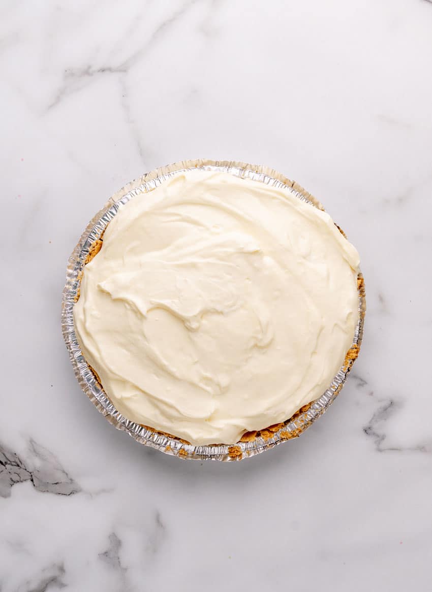 a homemade banana cream pie in a disposable pie pan on a marble countertop