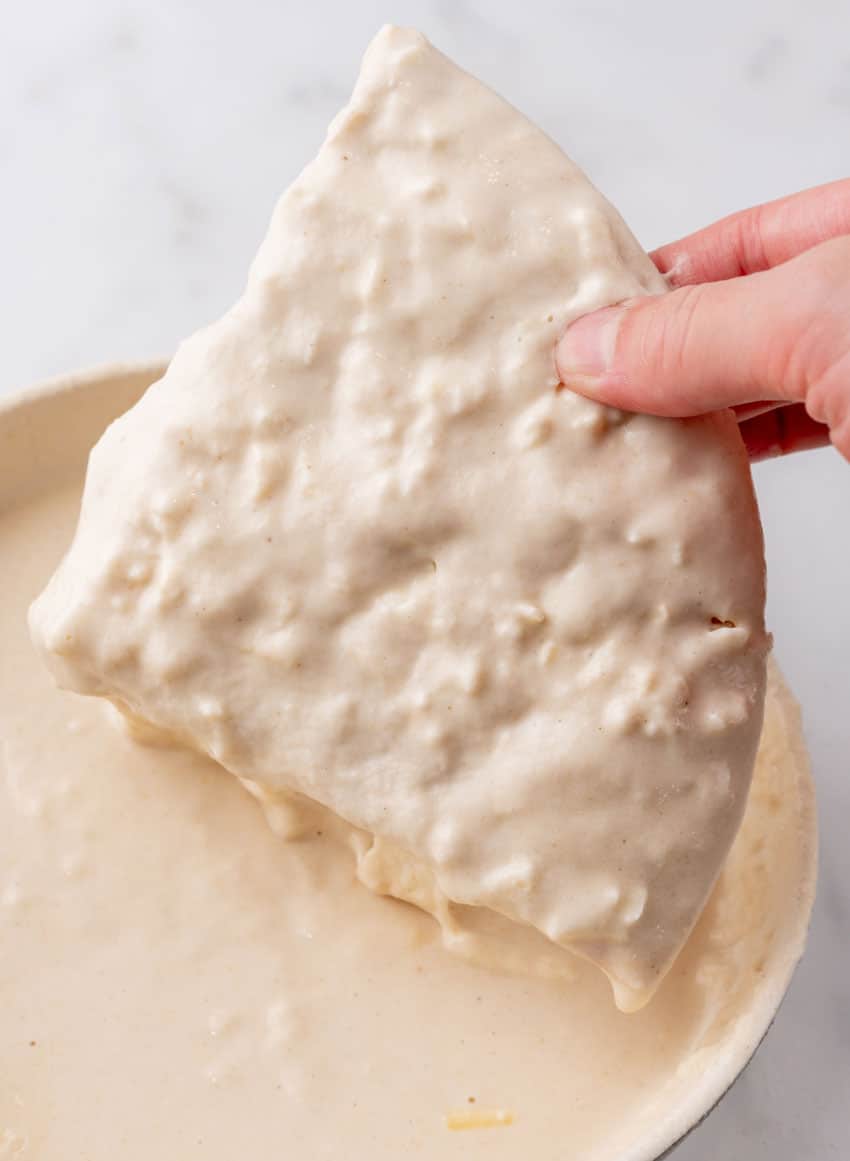 a hand holding up a piece of frozen pizza dipped in beer batter