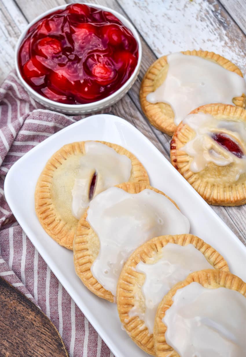 a row of air fried glazed cherry hand pies on a narrow white serving tray