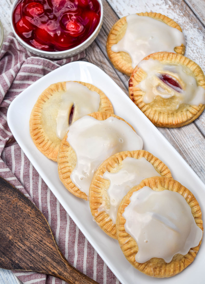 a row of air fried glazed cherry hand pies on a narrow white serving tray