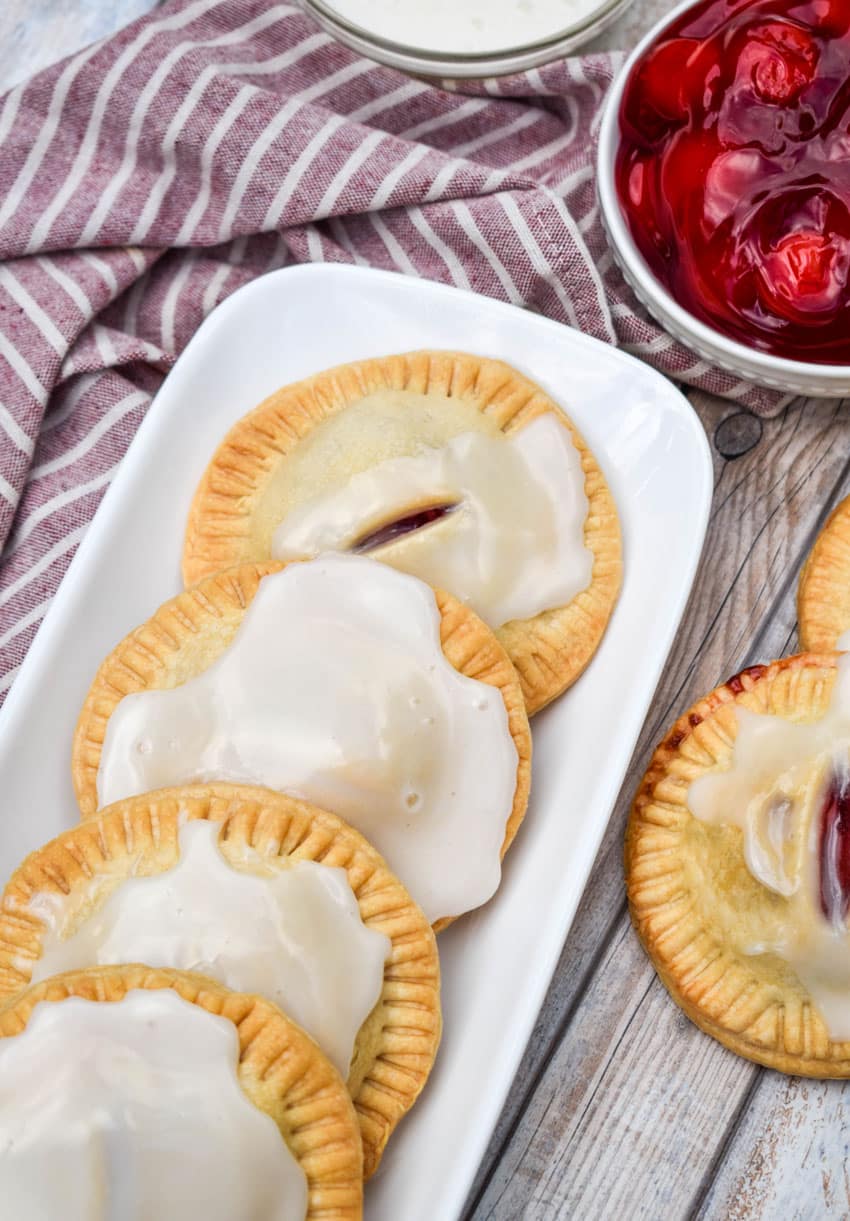 a row of air fried glazed cherry hand pies on a narrow white serving tray