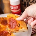 a hand holding up a small slice of a copycat pizza hut personal pan pizza