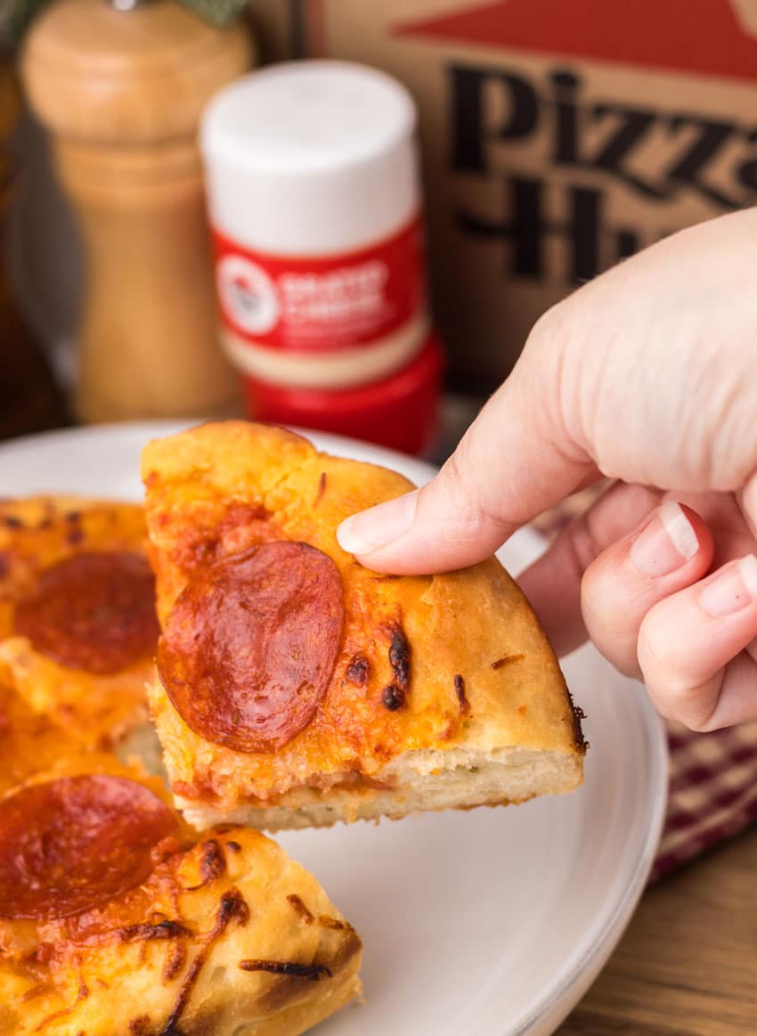 a hand holding up a small slice of a copycat pizza hut personal pan pizza