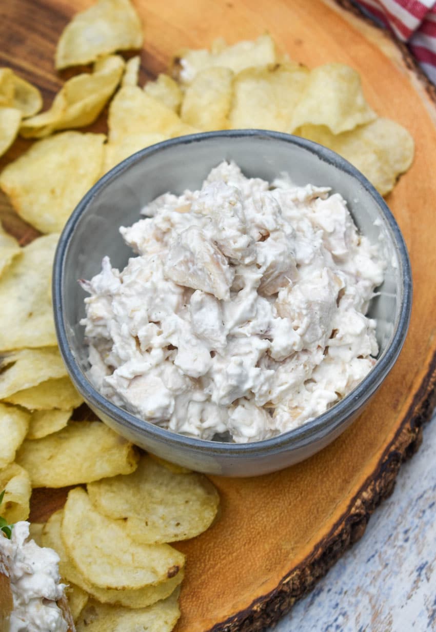 creamy french onion dip chicken salad in a small gray bowl surrounded by potato chips on a wooden cutting board