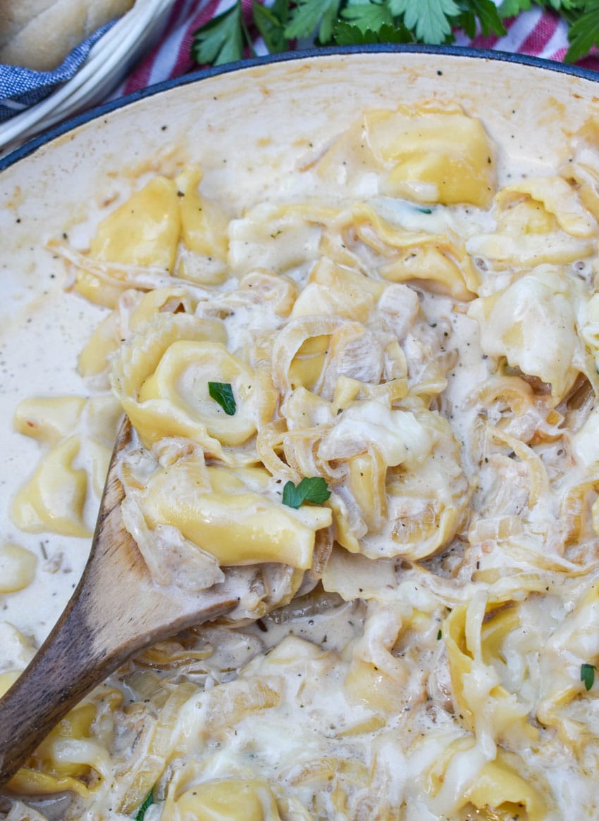 a wooden spoon scooping creamy french onion tortellini out of a cast iron skillet