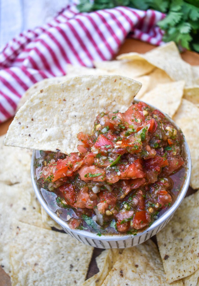 a tortilla chip scooping easy salsa fresca out of a small white bowl