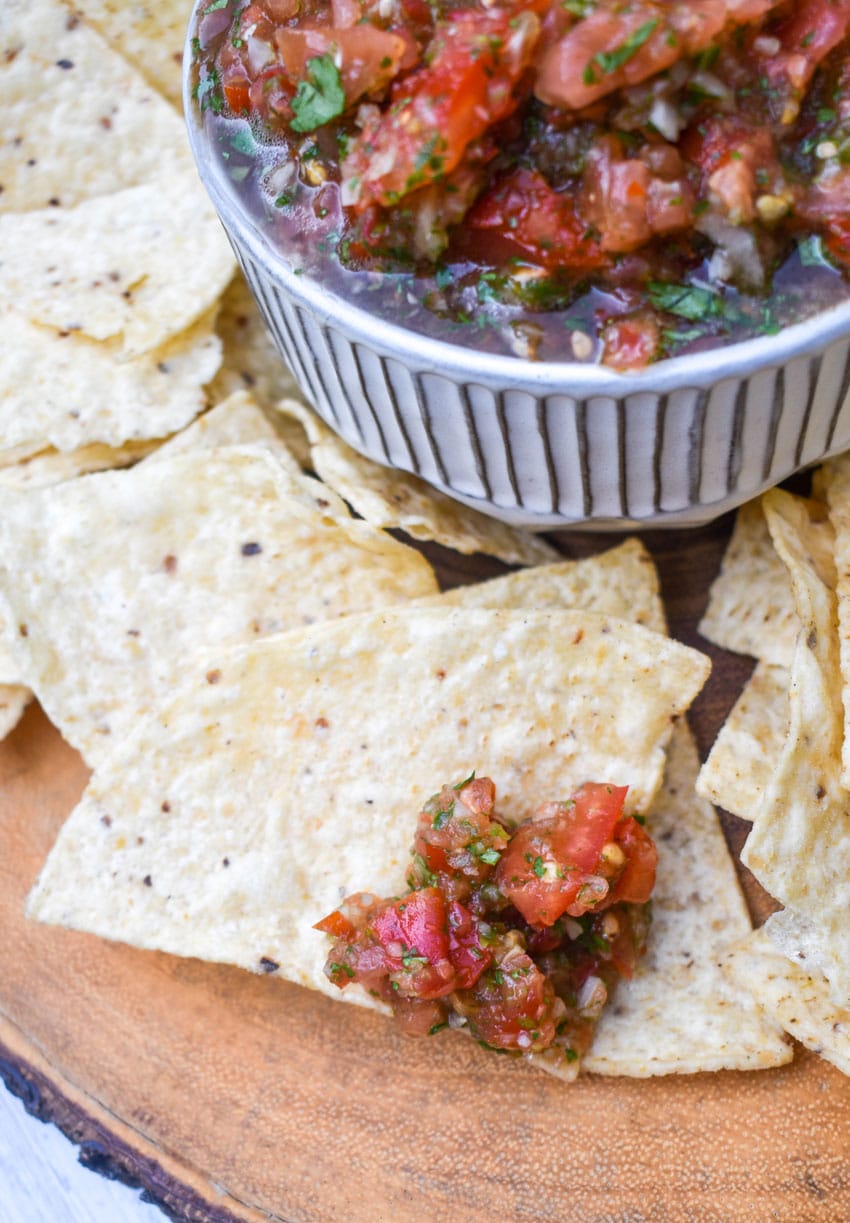 a tortilla chip topped with easy salsa fresca resting on a wooden cutting board
