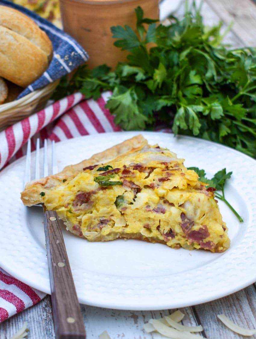 a slice of a baked reuben quiche on a small white plate with a fork resting on the side