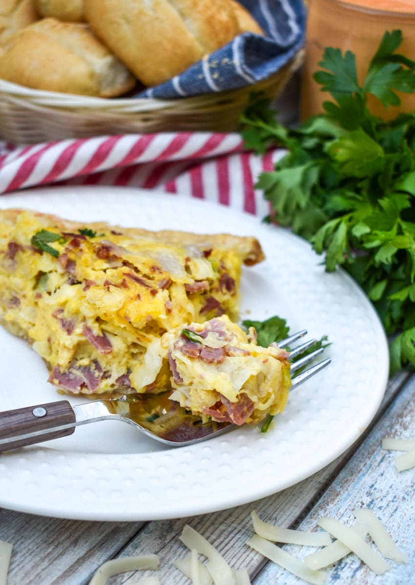 a fork holding a bite of reuben quiche resting on a the edge of a small white plate
