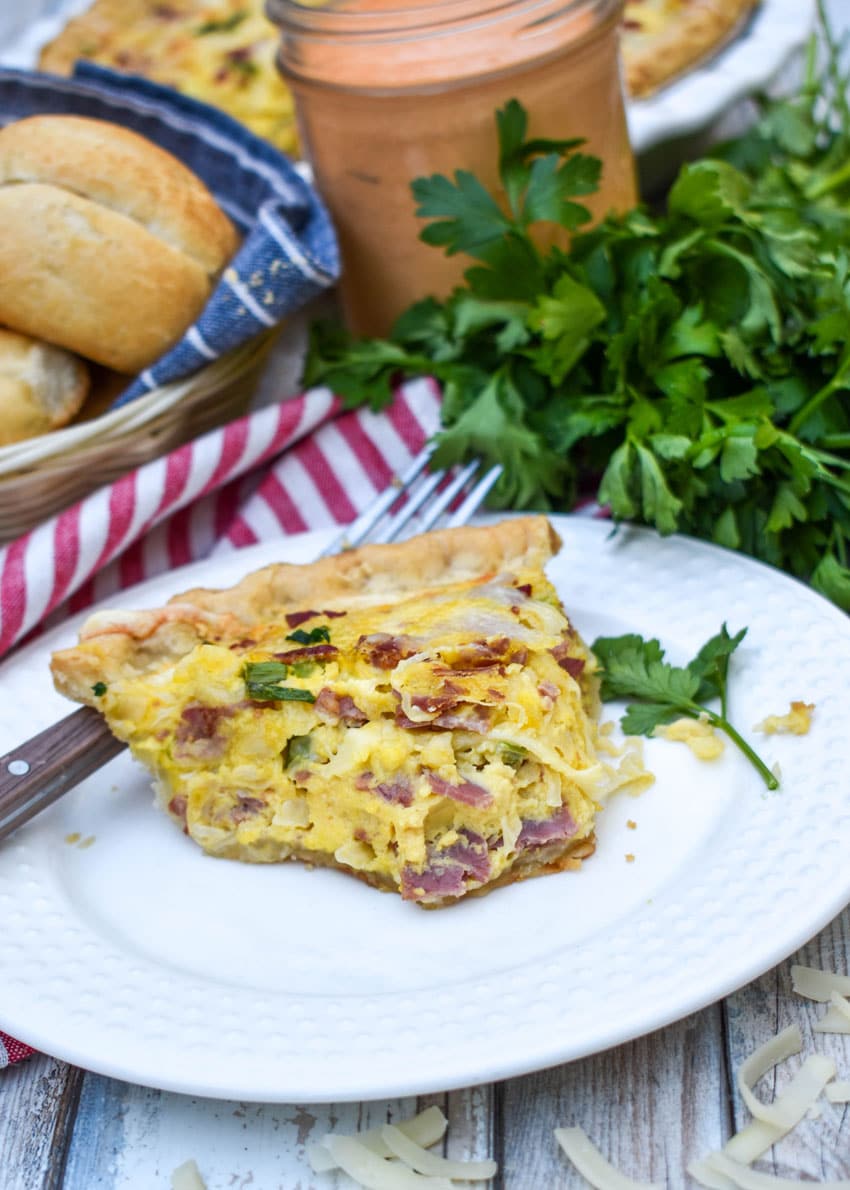 a slice of a baked reuben quiche on a small white plate with a fork resting on the side