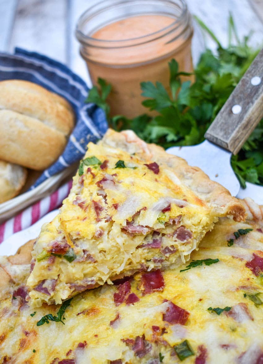 a wooden handled pie server holding up a slice of reuben quiche