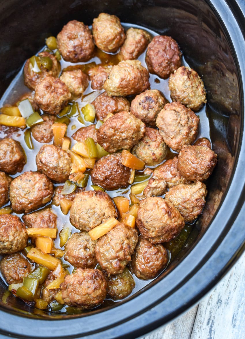 sweet and sour meatballs in the black bowl of a slow cooker