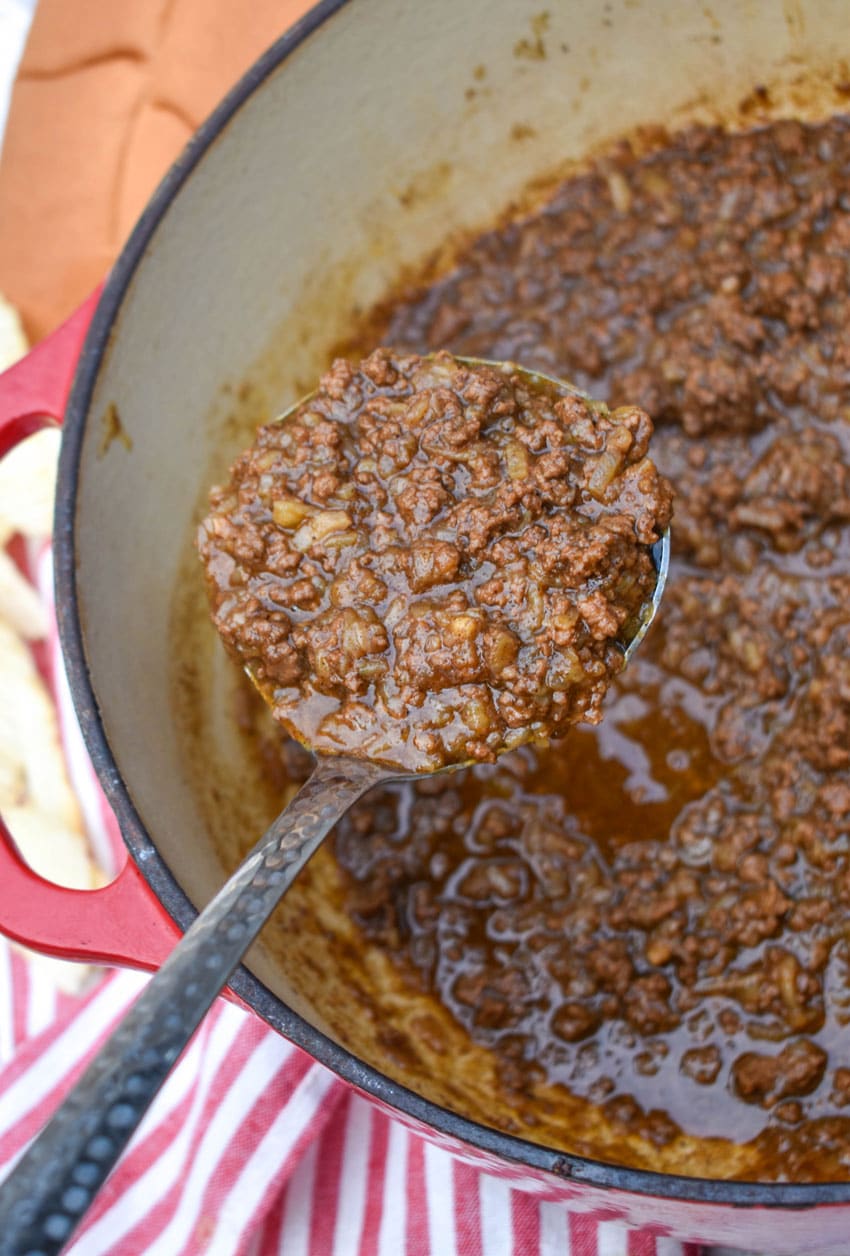 a silver ladle holding up a scoop of homemade spicy hot dog chili
