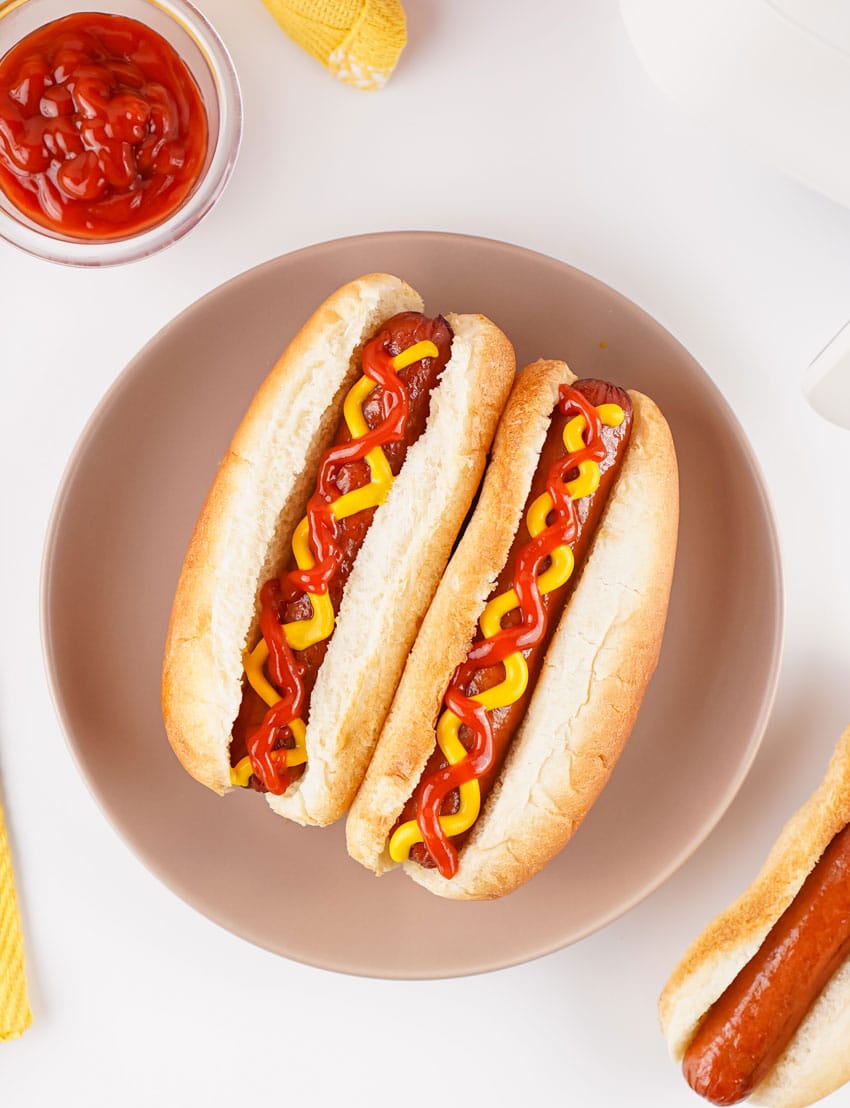 two air fryer hot dogs topped with ketchup and mustard in fluffy buns on a gray plate