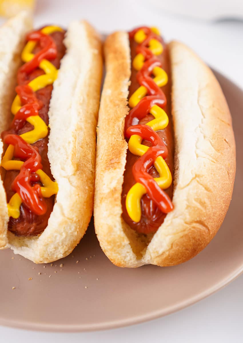 two air fryer hot dogs topped with ketchup and mustard in fluffy buns on a gray plate