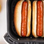 two air fried hot dogs in buns in the basket of an air fryer