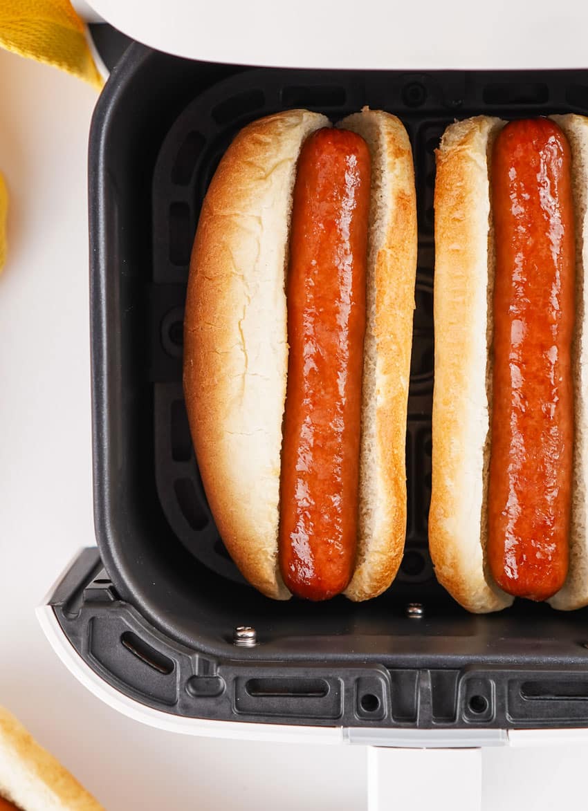 two air fried hot dogs in buns in the basket of an air fryer