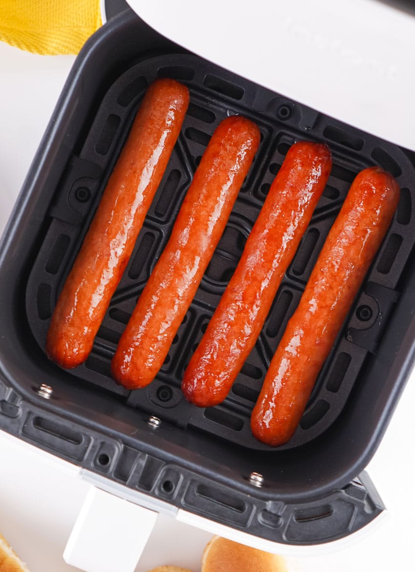 four cooked hot dogs arranged in a row in the basket of an air fryer