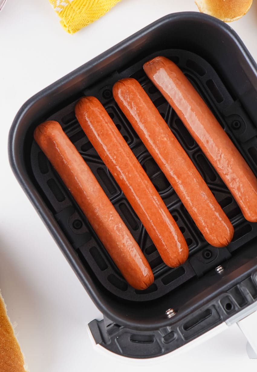 four uncooked hot dogs arranged in a row in the basket of an air fryer