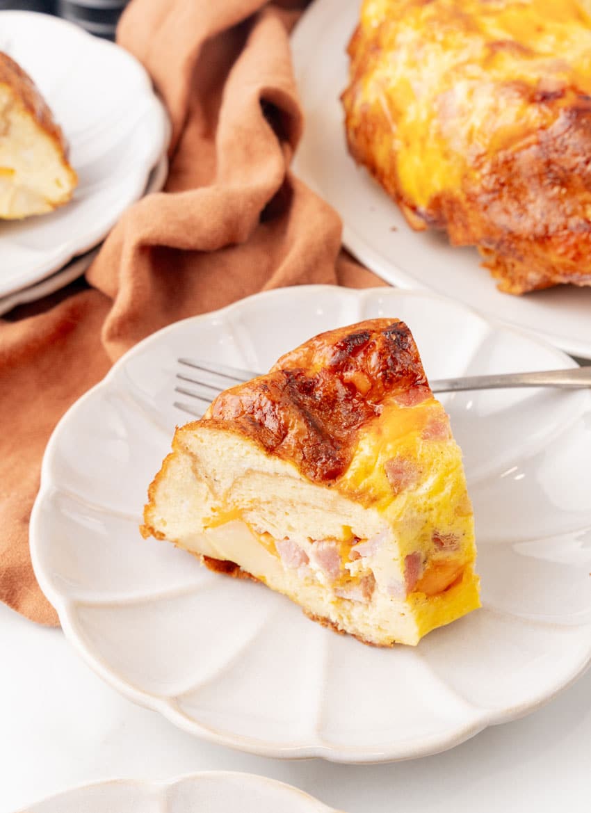a slice of a breakfast bundt bake on a white plate with a silver fork resting on the side