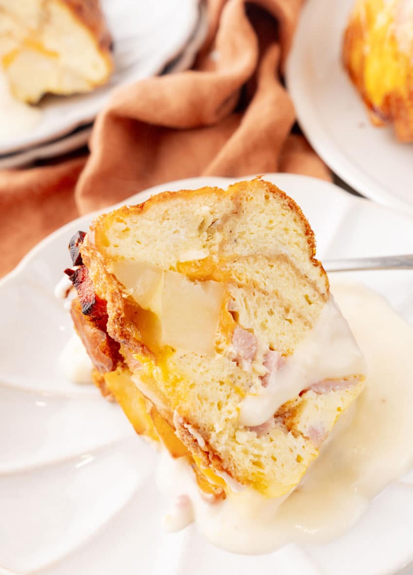 a slice of a breakfast bundt bake on a white plate with a silver fork resting on the side