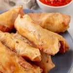 a stack of pepperoni spring rolls on a gray plate with a cup of marinara sauce on the side for dipping