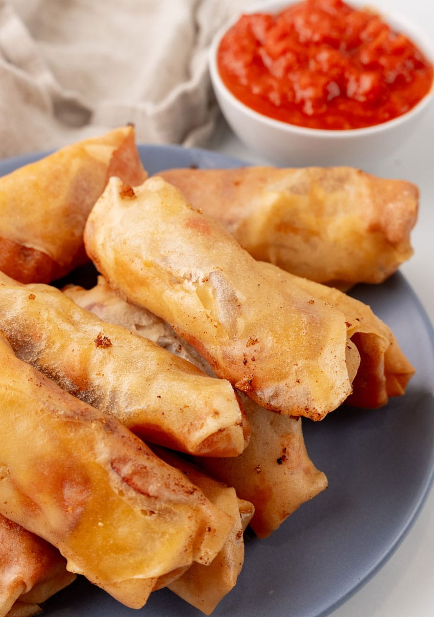 a stack of pepperoni spring rolls on a gray plate with a cup of marinara sauce on the side for dipping