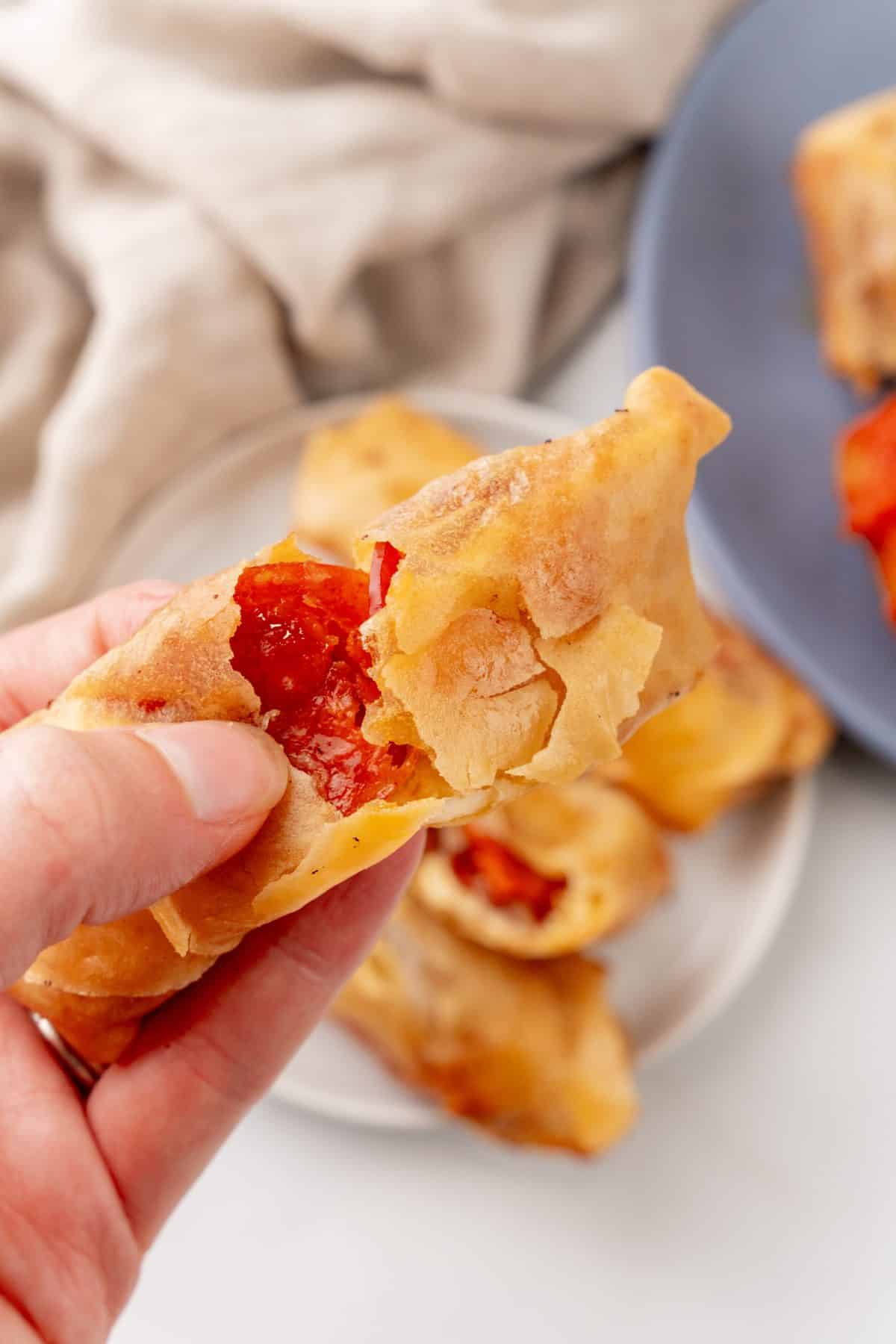 a hand holding up and pulling a part a fried pepperoni spring roll