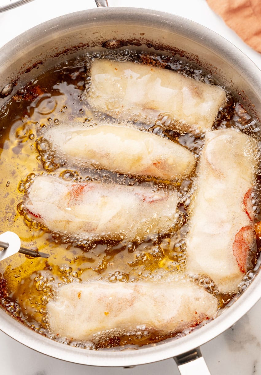 cheese and pepperoni filled egg rolls frying in a pot of hot oil