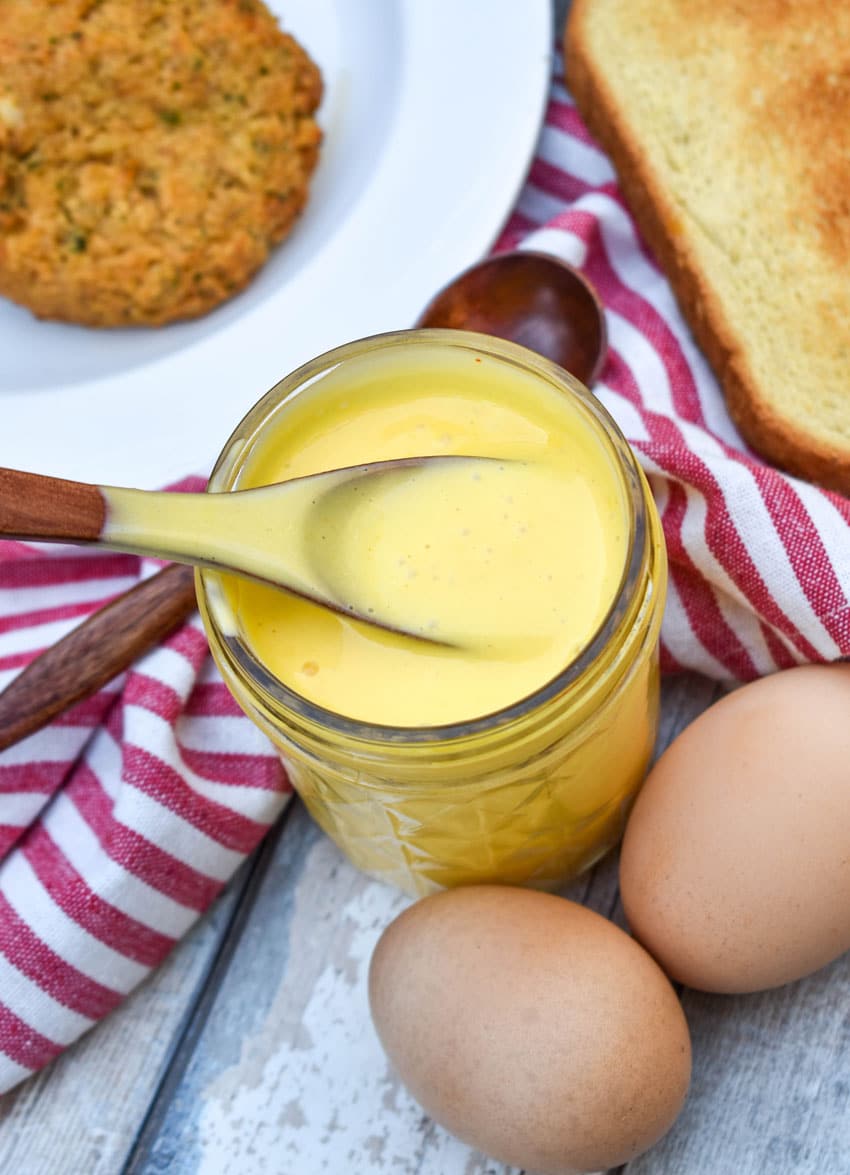 a wooden spoon scooping homemade hollandaise sauce out of a small glass jar