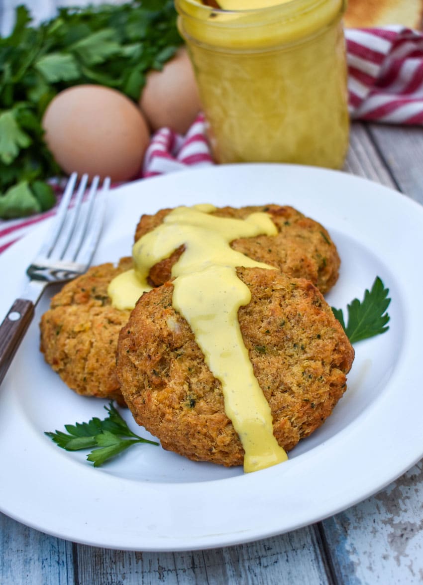three crab cakes topped with blender hollandaise sauce on a small white plate