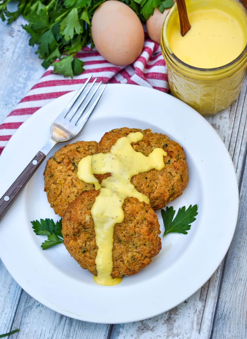 three crab cakes topped with homemade hollandaise sauce on a small white plate