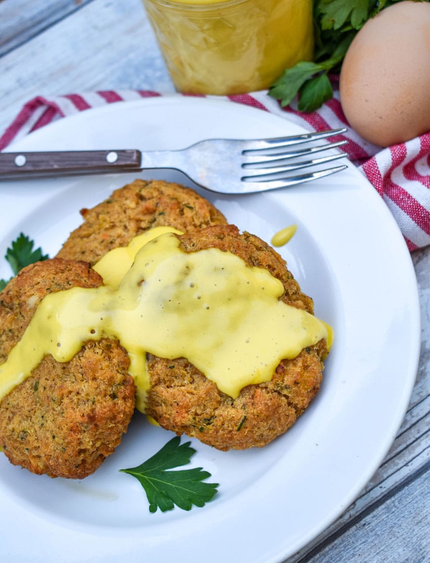 three crab cakes topped with blender hollandaise sauce on a small white plate