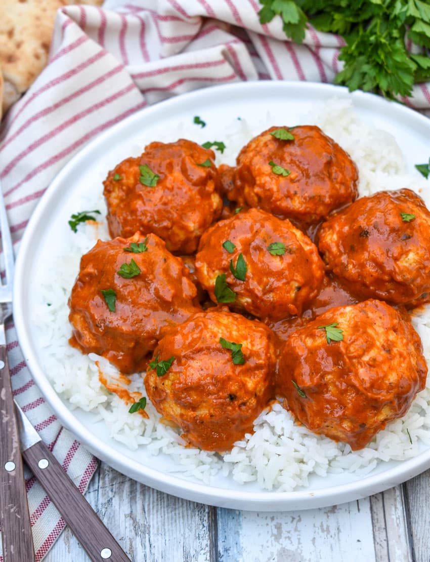 butter chicken meatballs over steamed white rice on a white plate