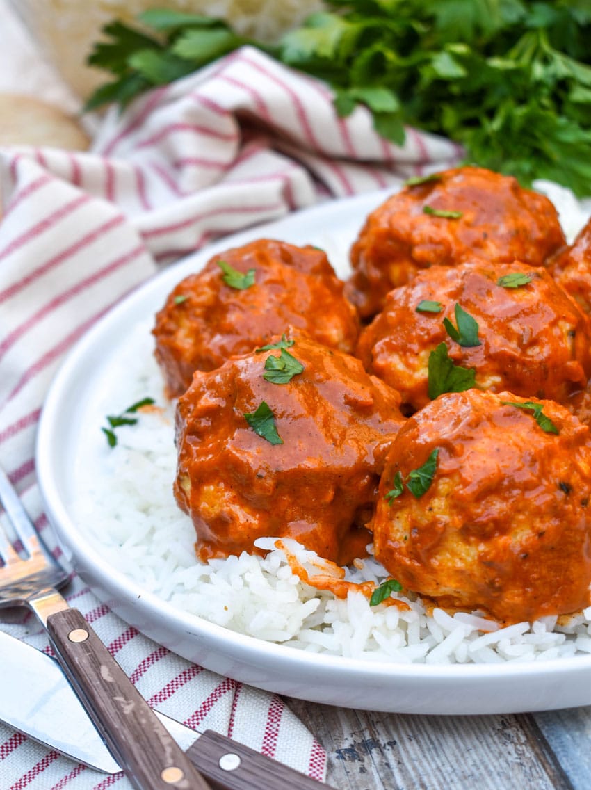 butter chicken meatballs over steamed white rice on a white plate