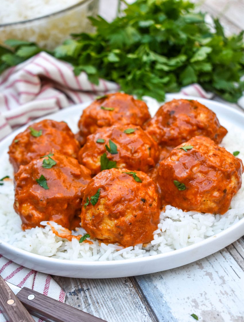 butter chicken meatballs over steamed white rice on a white plate