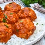 butter chicken meatballs over steamed white rice on a white plate
