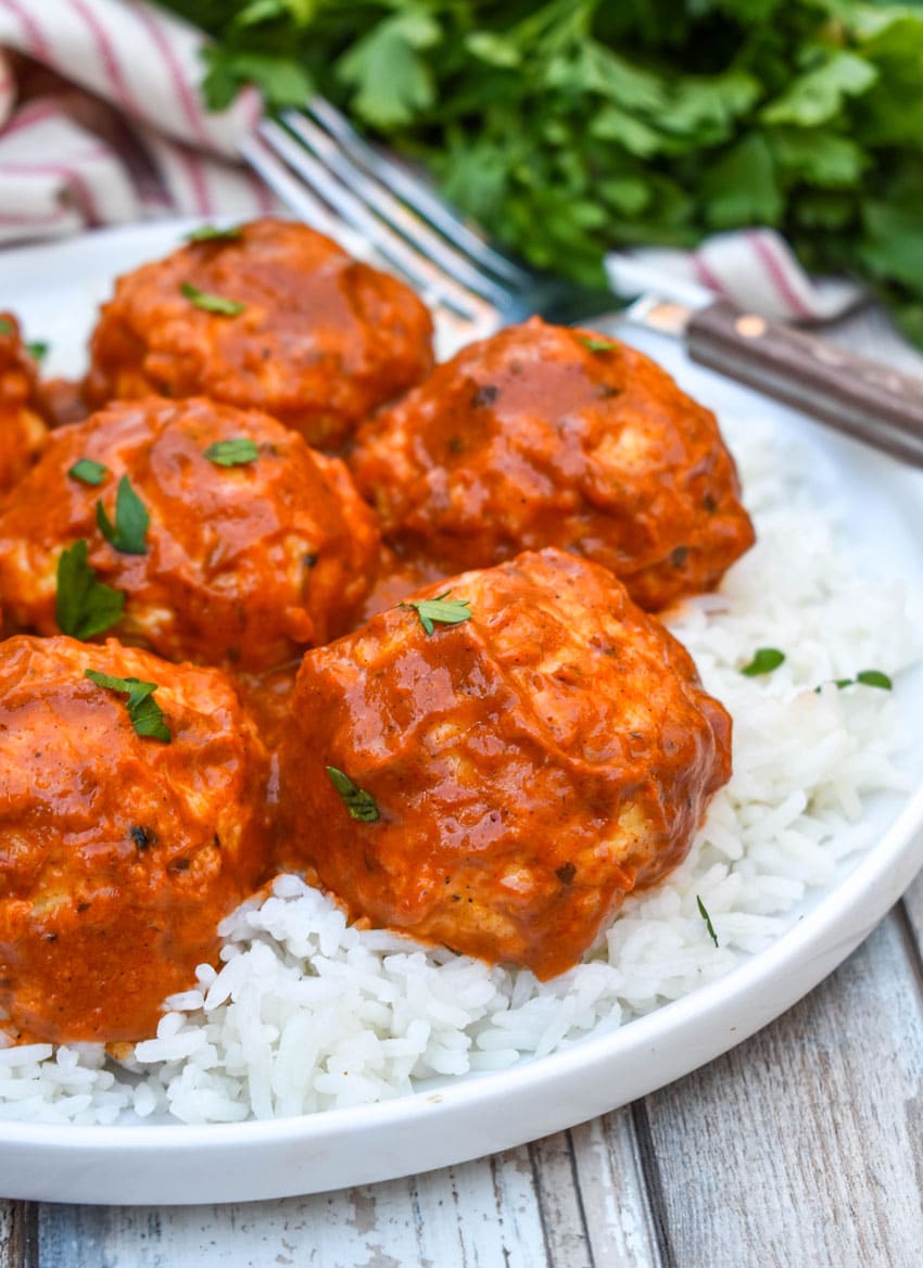butter chicken meatballs over steamed white rice on a white plate