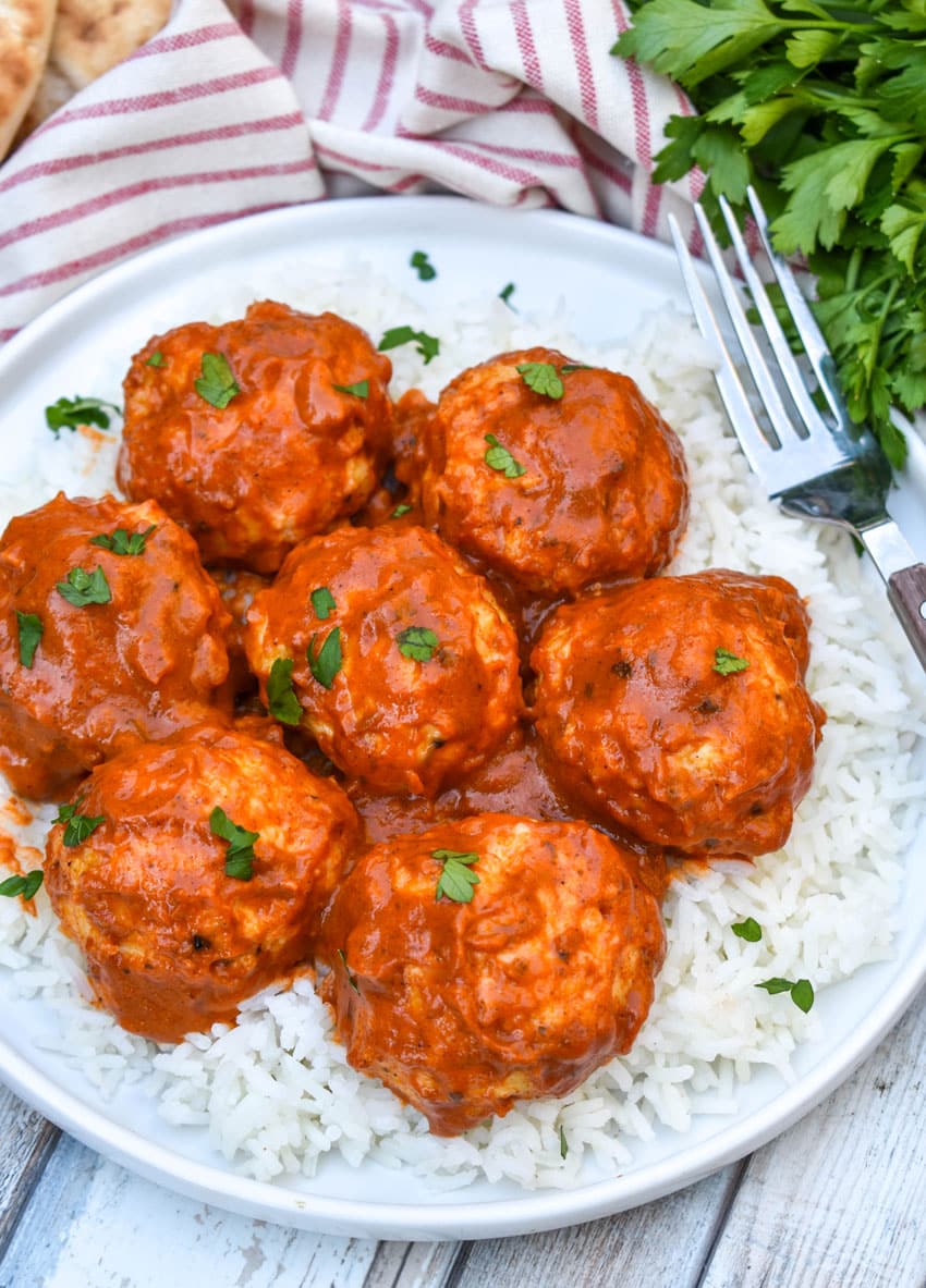 butter chicken meatballs over steamed white rice on a white plate