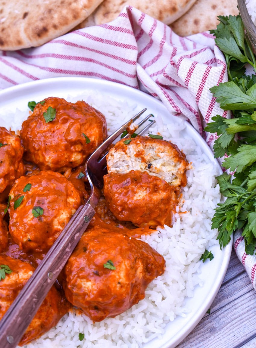 butter chicken meatballs over steamed white rice on a white plate
