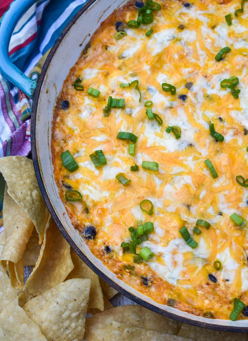 cheesy chicken enchilada dip in a cast iron skillet surrounded by tortilla chips