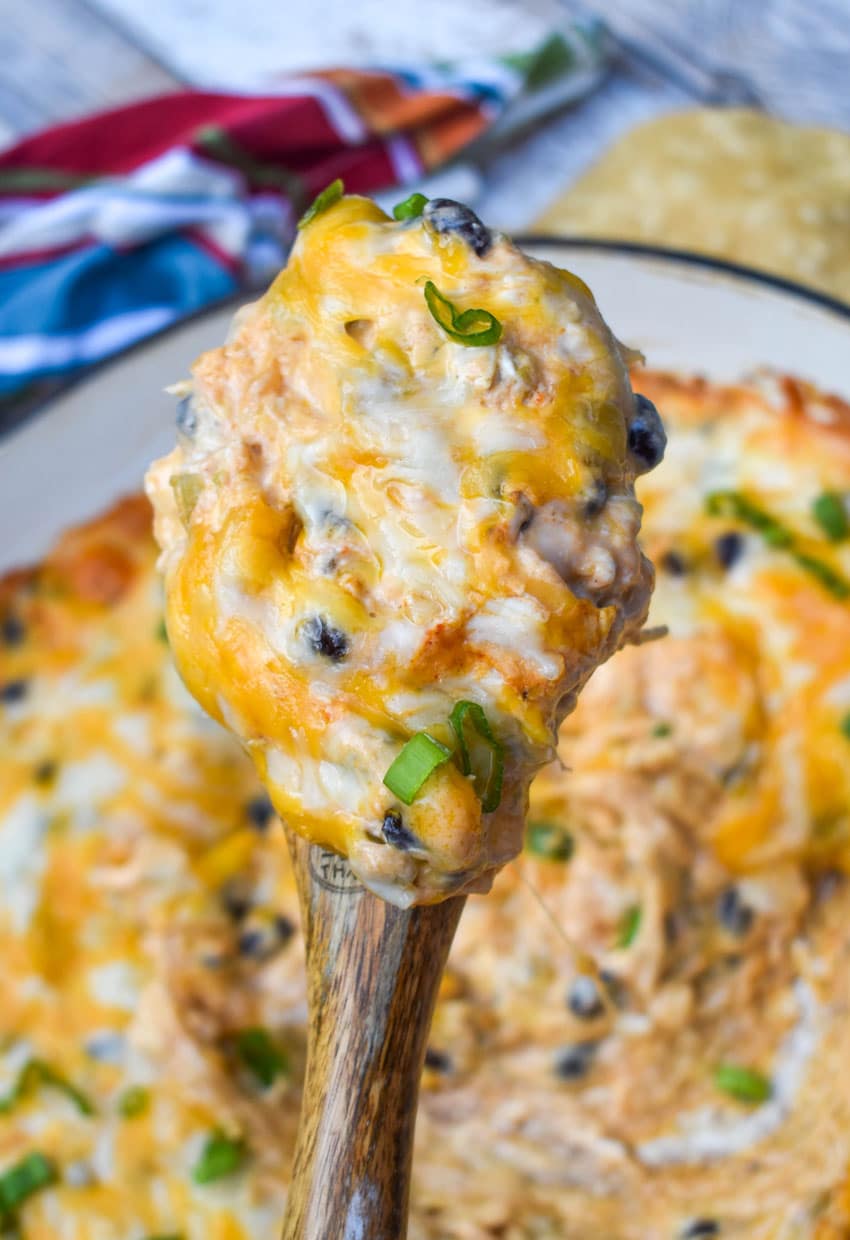 a wooden spoon holding up a scoop of cheesy chicken enchilada dip