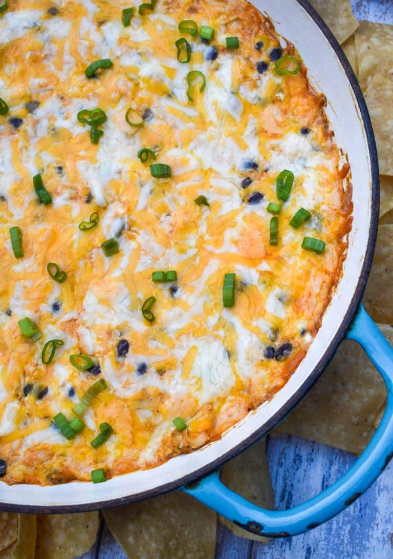 cheesy chicken enchilada dip in a cast iron skillet surrounded by tortilla chips