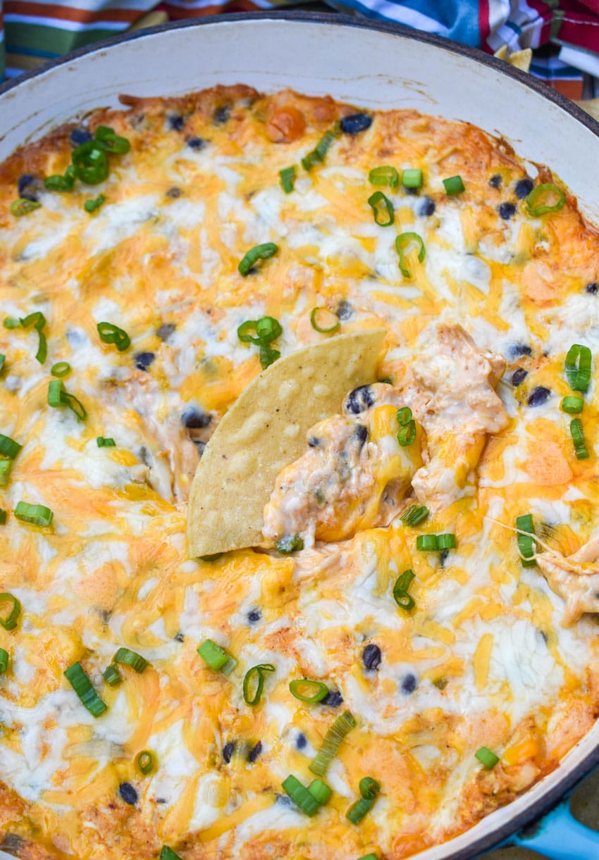 a tortilla chip scooping cheesy chicken enchilada dip out of a cast iron skillet