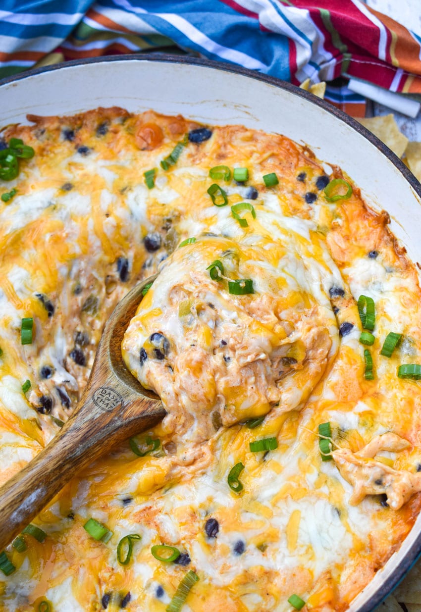 a wooden spoon scooping cheesy chicken enchilada dip out of a cast iron skillet