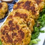a row of cornbread stuffing crab cakes resting on green lettuce leaves on a white platter