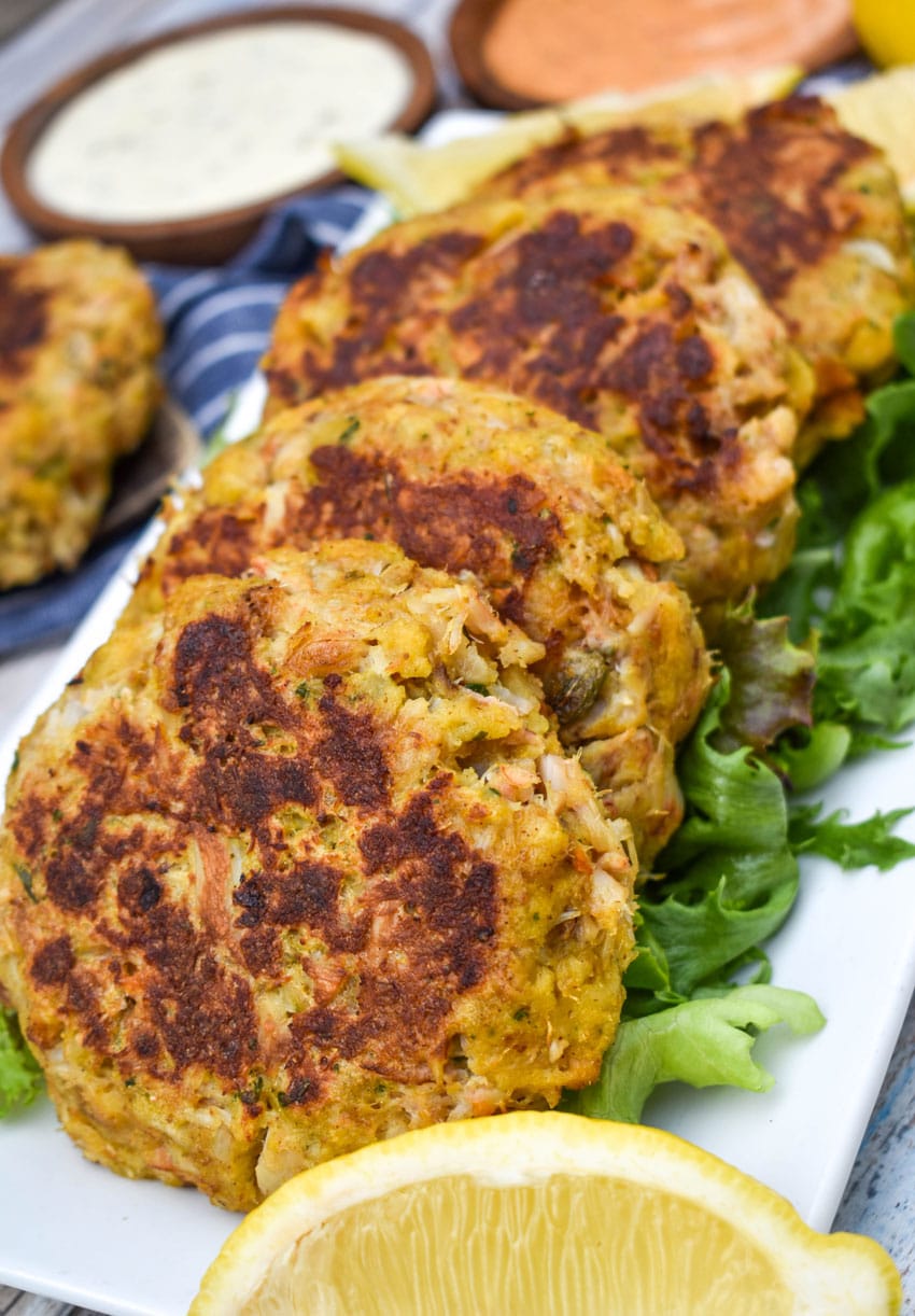 a row of cornbread stuffing crab cakes resting on green lettuce leaves on a white platter