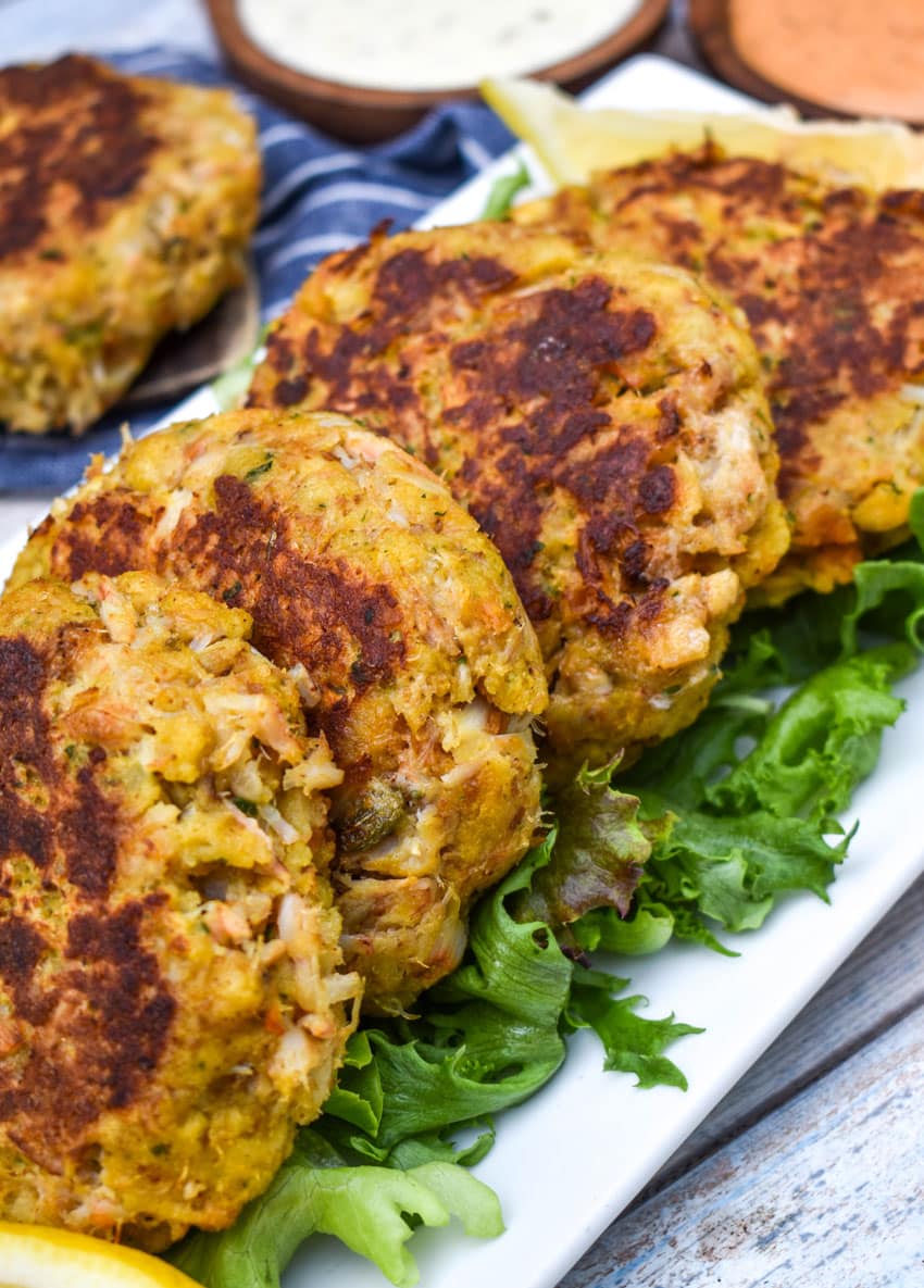 a row of cornbread stuffing crab cakes resting on green lettuce leaves on a white platter