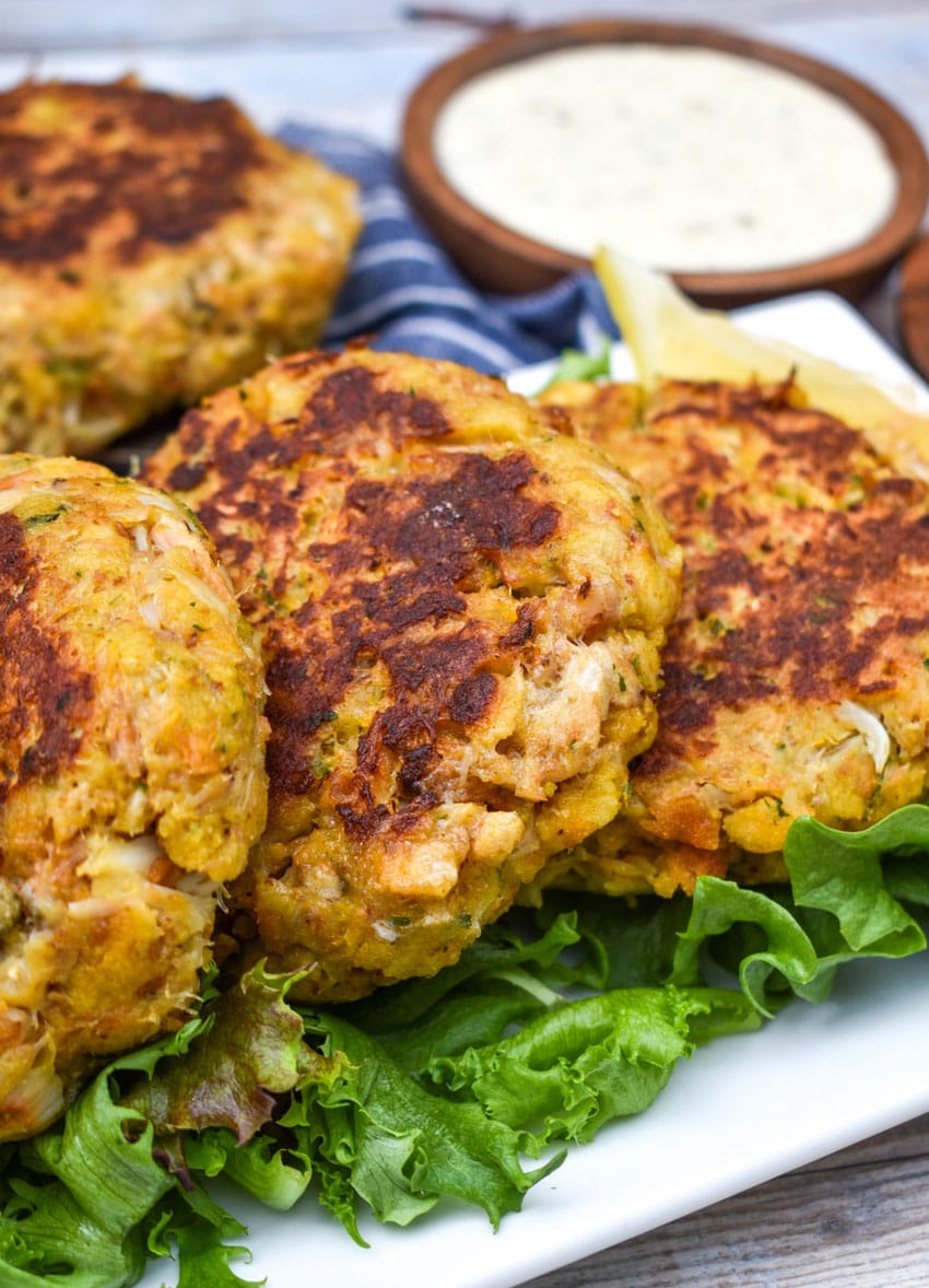a row of cornbread stuffing crab cakes resting on green lettuce leaves on a white platter