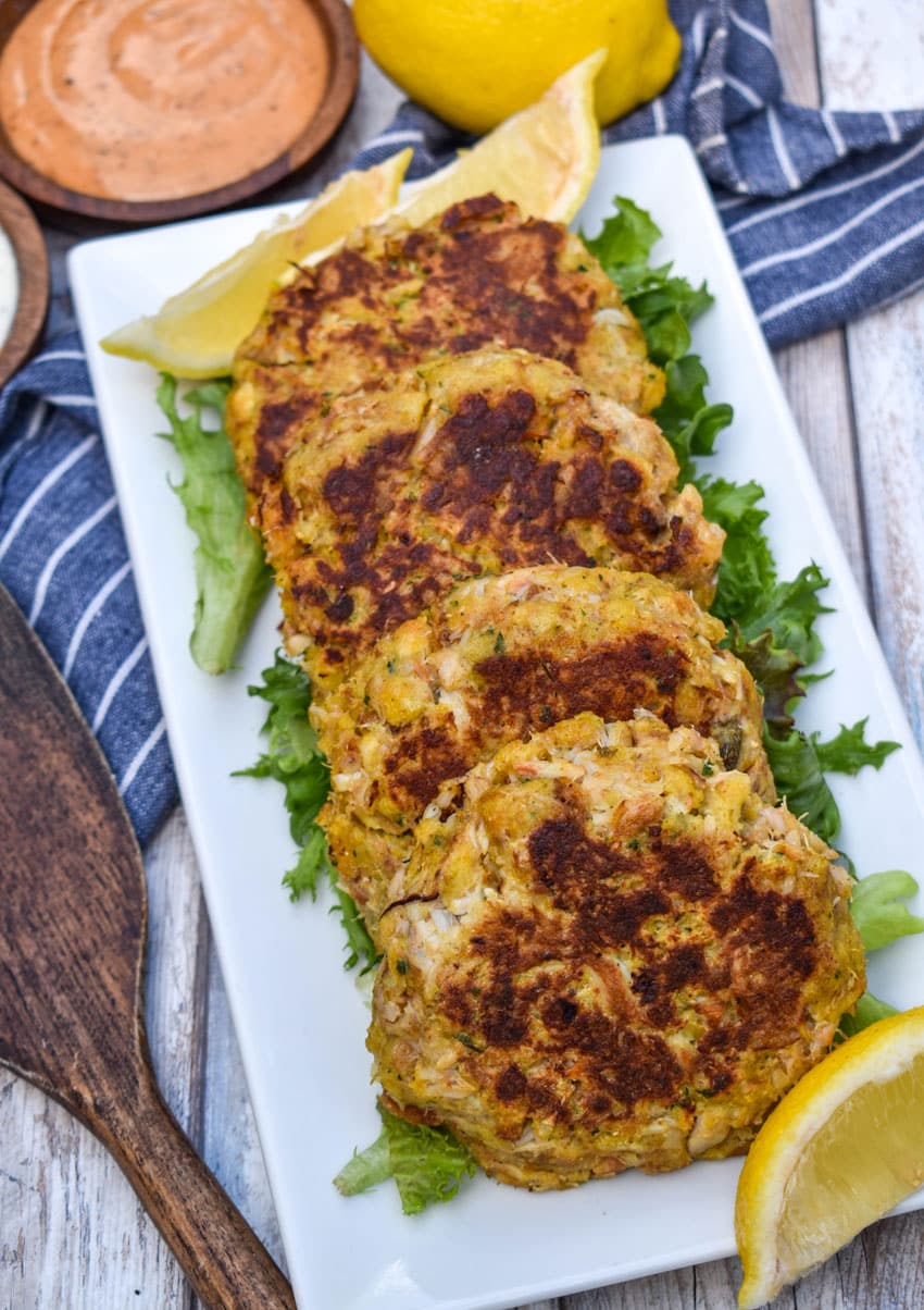 a row of cornbread stuffing crab cakes resting on green lettuce leaves on a white platter
